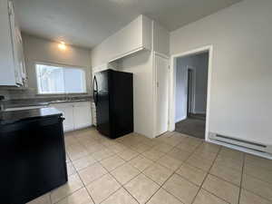 Kitchen featuring white cabinets, black appliances, light tile patterned floors, and a baseboard heating unit