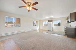 Unfurnished living room featuring ceiling fan, light wood-type flooring, and a baseboard heating unit