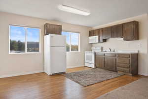 Kitchen with dark brown cabinets, light hardwood / wood-style flooring, white appliances, and sink