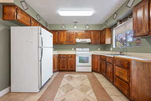 Kitchen featuring a textured ceiling, sink, light tile patterned floors, and white appliances