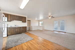 Kitchen featuring light wood-type flooring, dark brown cabinets, white appliances, ceiling fan, and sink