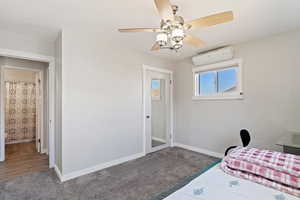 Carpeted bedroom featuring a wall mounted AC and ceiling fan