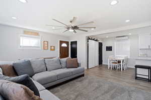 Living room with a barn door, ceiling fan, hardwood style tile flooring, and a wall mounted air conditioner