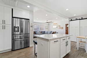 Kitchen with a barn door, stainless steel fridge with ice dispenser, white cabinets, and wood-type tile flooring