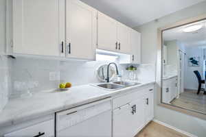 Kitchen featuring white cabinetry, sink, light hardwood / wood-style flooring, white dishwasher, and decorative backsplash