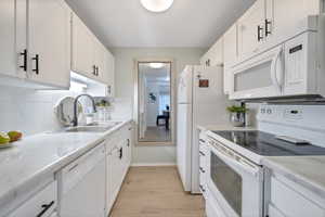 Kitchen with white appliances, sink, tasteful backsplash, light hardwood / wood-style floors, and white cabinetry