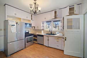 Kitchen featuring an inviting chandelier, white cabinets, sink, light wood-type flooring, and stainless steel appliances