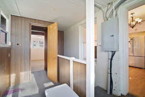 Hallway with a chandelier, electric panel, light hardwood / wood-style flooring, and wood walls