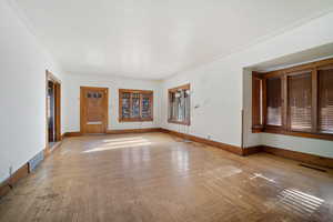 Unfurnished living room with ornamental molding and light parquet floors