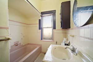 Bathroom featuring vaulted ceiling, a washtub, tile walls, and sink