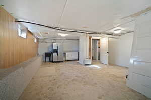 Basement with stainless steel fridge with ice dispenser, sink, light carpet, and wood walls