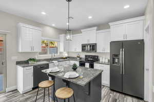 Kitchen featuring white cabinetry, sink, decorative light fixtures, a kitchen island, and black appliances