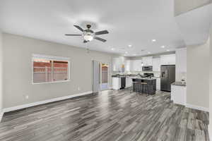 Kitchen featuring a center island, white cabinets, hanging light fixtures, appliances with stainless steel finishes, and a kitchen bar