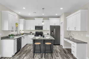 Kitchen featuring light stone countertops, appliances with stainless steel finishes, a center island, and white cabinetry