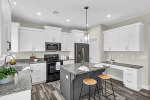 Kitchen featuring white cabinets, stone countertops, a kitchen island, dark hardwood / wood-style flooring, and stainless steel appliances