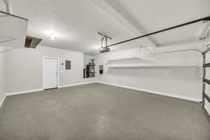 Garage featuring strapped water heater, a garage door opener, and electric panel