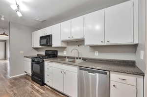 Kitchen featuring sink, hardwood / wood-style flooring, white cabinetry, and black appliances