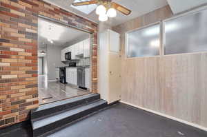 Kitchen featuring brick wall, white cabinetry, wood walls, and black appliances