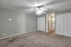 Unfurnished bedroom featuring carpet flooring, ceiling fan, and two closets