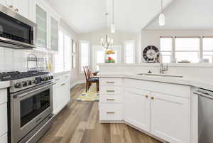 Kitchen with white cabinetry, sink, stainless steel appliances, vaulted ceiling, and light wood-type flooring