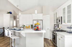 Kitchen featuring hardwood / wood-style floors, hanging light fixtures, decorative backsplash, appliances with stainless steel finishes, and white cabinetry