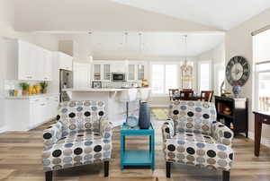 Living room featuring vaulted ceiling, light wood-type flooring, and a chandelier