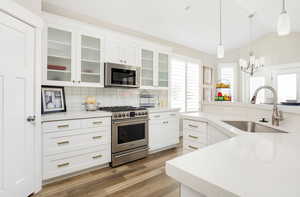 Kitchen featuring stainless steel appliances, sink, hardwood / wood-style flooring, white cabinets, and lofted ceiling