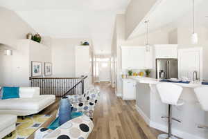 Kitchen with high vaulted ceiling, high end refrigerator, white cabinets, decorative light fixtures, and light hardwood / wood-style floors