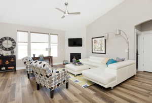 Living room with ceiling fan, a stone fireplace, wood-type flooring, and vaulted ceiling