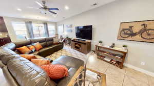 Tiled living room with ceiling fan with notable chandelier and lofted ceiling