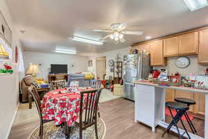 Kitchen with light brown cabinets, ceiling fan, light wood-type flooring, a breakfast bar area, and stainless steel refrigerator