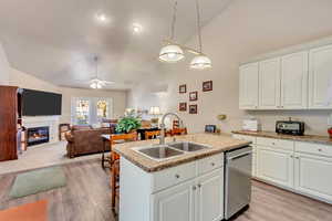 Kitchen featuring dishwasher, white cabinets, lofted ceiling, and sink