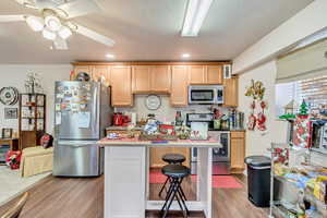 Kitchen with light brown cabinets, light wood-type flooring, stainless steel appliances, and a kitchen breakfast bar