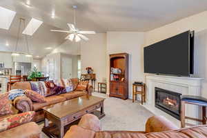 Living room featuring light carpet, lofted ceiling with skylight, ceiling fan, and a fireplace