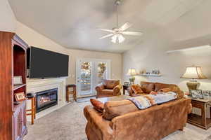 Living room with ceiling fan, a fireplace, light colored carpet, and vaulted ceiling