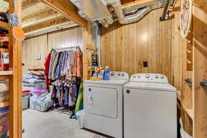 Clothes washing area featuring washer and clothes dryer and wood walls