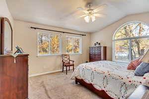 Bedroom featuring light carpet, multiple windows, lofted ceiling, and ceiling fan