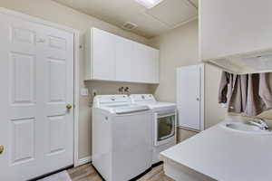 Clothes washing area with cabinets, separate washer and dryer, light hardwood / wood-style flooring, and sink