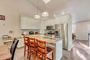 Kitchen with appliances with stainless steel finishes, light wood-type flooring, hanging light fixtures, lofted ceiling, and an island with sink