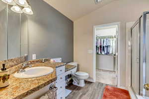 Bathroom with hardwood / wood-style floors, vaulted ceiling, toilet, vanity, and a shower with shower door