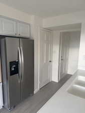 Kitchen with sink, white cabinets, wood-type flooring, and stainless steel refrigerator with ice dispenser