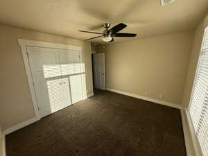 Unfurnished bedroom with dark colored carpet, ceiling fan, a textured ceiling, and a closet