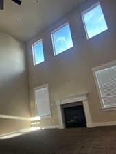 Unfurnished living room featuring ceiling fan, carpet floors, and a high ceiling