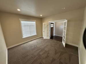 Unfurnished room with french doors, dark carpet, and a textured ceiling