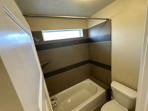 Bathroom featuring a textured ceiling, tiled shower / bath combo, and toilet