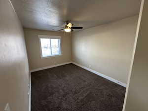 Carpeted spare room featuring ceiling fan and a textured ceiling