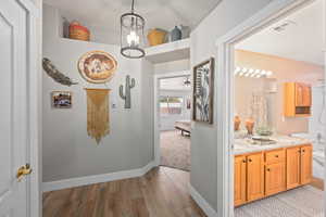 Corridor with light wood-type flooring and an inviting chandelier