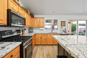 Kitchen with sink, light hardwood / wood-style flooring, decorative backsplash, light stone countertops, and stainless steel appliances