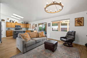 Living room with a notable chandelier, light hardwood / wood-style floors, lofted ceiling, and sink