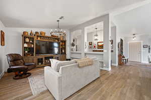 Living room featuring light hardwood / wood-style floors, lofted ceiling, and a notable chandelier